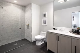 Luxe baths include a custom grey oak bathroom vanity with marble counters, frameless glass-enclosed showers with marble tile wet walls and oversized porcelain tile flooring.