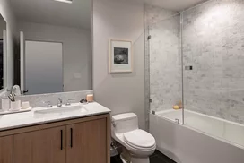 Luxe baths include a custom grey oak bathroom vanity with marble counters, frameless glass-enclosed showers with marble tile wet walls and oversized porcelain tile flooring.