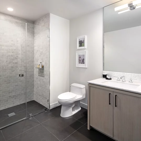 Luxe baths include a custom grey oak bathroom vanity with marble counters, frameless glass-enclosed showers with marble tile wet walls and oversized porcelain tile flooring.