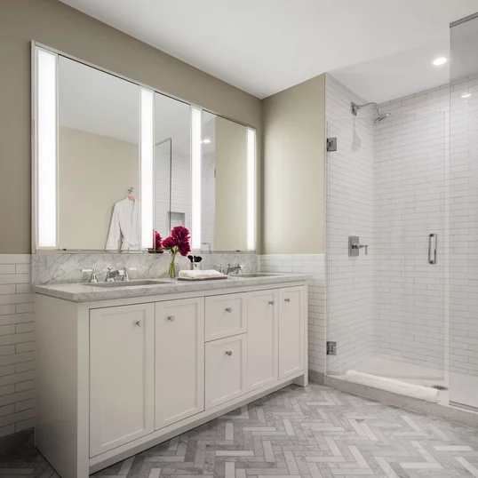 Luxuriate in master baths featuring white natural stone vanity, Kohler fixtures and accessories in polished chrome, and natural stone tile floor in white herringbone tile.